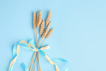 Fototapeta premium Ears of wheat with ribbons in colors of Ukrainian national flag on light blue background, top view. Space for text