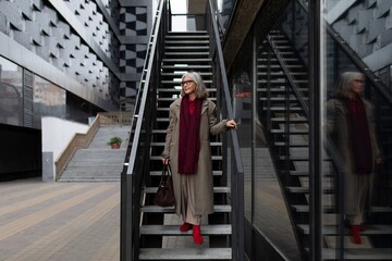 Middle-aged businesswoman confidently walks down the stairs outside a modern building in stylish attire during an urban afternoon