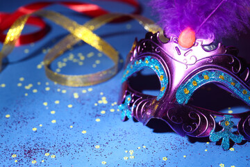 Beautiful bright carnival mask, ribbons and confetti on blue background, closeup