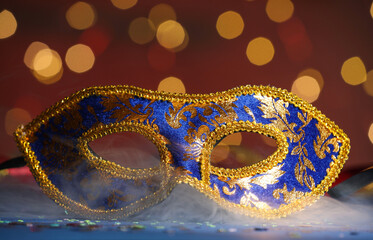 Beautiful carnival mask and confetti in smoke on color background, closeup