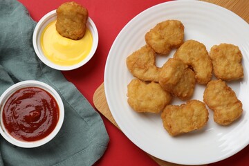 Delicious chicken nuggets and sauces on red background, flat lay