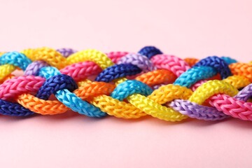 Braided colorful ropes on pink background, closeup. Unity concept