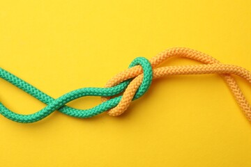 Colorful ropes tied in knot on yellow background, top view. Unity concept