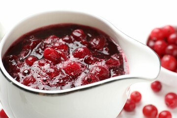 Tasty cranberry sauce in gravy boat and berries on table, closeup