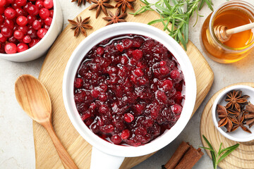 Tasty cranberry sauce in gravy boat, berries, honey and spices on light table, flat lay