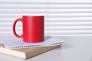 One blank red ceramic mug and notebooks on white table. Mockup for design