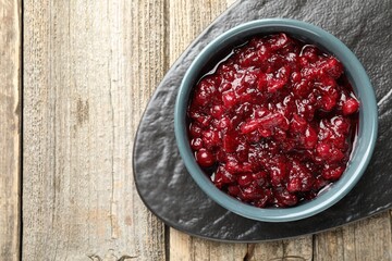 Tasty cranberry sauce in bowl on wooden table, top view. Space for text