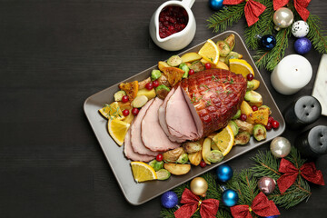 Tasty baked ham served with vegetables and oranges on black wooden table, flat lay