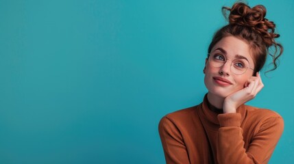 Fototapeta premium A stylish woman with her hand on her chin, posing against a vibrant blue wall. She is wearing fashionable glasses and a modern sweater.