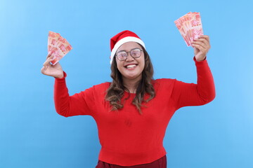 Young asian woman holding indonesia banknotes screaming proud, celebrating victory and success very excited with raised arm