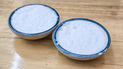 coconut milk custard in small porcelain cup (Thai dessert) in wooden dish on table.