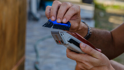A close-up shot of a man's hand cleaning an electric razor with a brush after shaving in the...