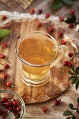 A cup of rose hip tea on a table with fresh rosehips