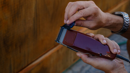 A close-up shot of a man's hand cleaning an electric razor with a brush after shaving in the tree-filled garden of his house on a sunny summer day