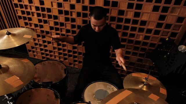Drummer energetically playing a drum set in a soundproofed studio with wooden acoustic panels, focused on creating rhythm.