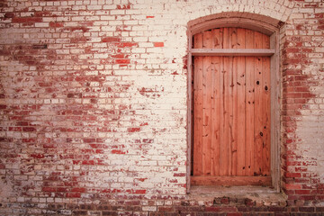 Freshly boarded up window set in wall with peeling paint on old bricks