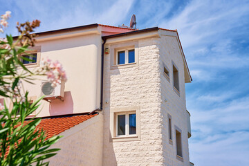 Modern Mediterranean house with red tile roof, white stone facade, and lush greenery under bright blue sky. Residential building at summer day