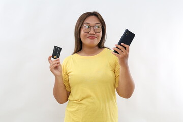 Smiling asian woman, lady in suit thinking, holding smartphone and credit card, plan to buy something online, shopping with mobile phone, white background