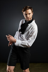 A stylish dandy poses confidently in a dark studio setting, exuding charm and elegance
