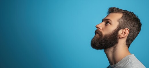 Naklejka premium Profile view of man with beard against blue background, thoughtful expression