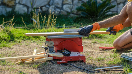A middle-aged man cutting timber with a circular saw in the garden of his house on a summer day