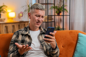 Sad displeased Caucasian man using smartphone typing browsing, loses becoming surprised sudden...