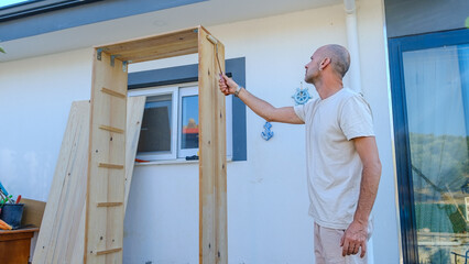 A middle-aged man varnishing a wooden cupboard with a paintbrush in the garden of his house on a summer day