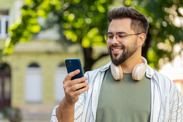 Happy successful satisfied Caucasian man young guy male tourist mobile phone user holding smartphone texting chatting social media tourist online GPS map outdoor urban city street. Town lifestyles.