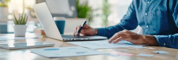 Business professional working on financial documents and laptop in a modern office environment