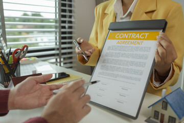 A man signs a contract after agreeing to buy a house with an agent. The agent explains the details of the contract to the buyer before signing it. Home purchase contract
