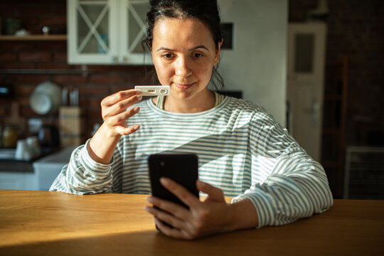Young woman showing positive pregnancy test to a smartphone in kitchen