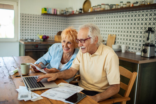 Happy senior couple playing bills online with credit card at home