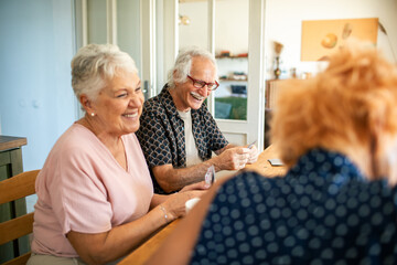 Senior friends playing with cards at kitchen table