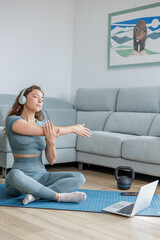 Obraz premium Beautiful young sports woman having fun listening to music on the mat while doing some stretching, meditation and strength exercises in her living room, positive energy, healthy life