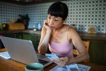 Stressed woman managing bills with laptop on kitchen desk