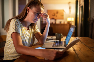 Woman stressed while reviewing bills and working on laptop at night