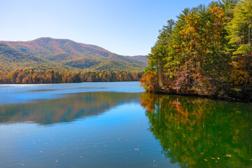 The Indian Boundary Lake in autumn, with vibrant red, yellow, orange, and green trees along the shoreline and the Unicoi mountains in the background. Cherohala Skyway in Tennessee. Horizontal