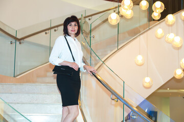 Adult brunette woman in a room with a beautiful interior climbs a luxurious staircase concept of success and well-being.