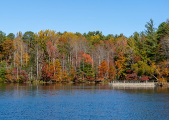 A view across the Indian Boundary Lake in autumn, vibrant red, yellow, and green trees line the...