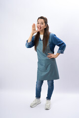 Young woman wearing apron, shouting open mouth, scream sharing hot news about sales discount with hands near mouth, white background, vertical portrait