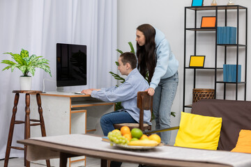 A woman is assisting a boy with a computer in their cozy and inviting living room space