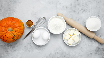 Baking ingredients including flour, butter, sugar, spices, eggs and pumpkin arranged on a gray background. Seasonal autumn baking