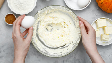 Woman breaks an egg into a bowl of dough. Ingredients for autumn baking
