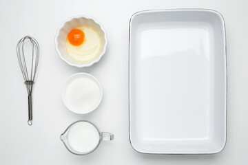 Empty white baking dish with ingredients for baking, including egg, milk, butter, sugar, and nuts...
