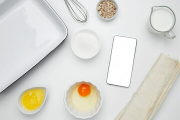 Cooking ingredients and smartphone with blank screen on a white background. For baking Crinkle Cake. Mockup design for recipe or food blog