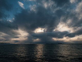 Dark clouds loom over the ocean during dusk, with rays of sunlight piercing through.