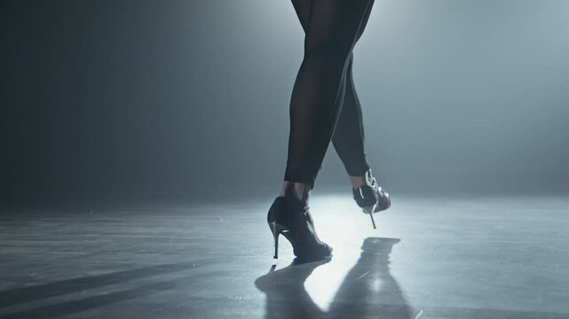 Dancer legs walking through dark studio. Young woman entering stage with smoke and lights on background. Young woman walking in high heels. Dance concept. Cinematic video. Tracking shot in 4K, UHD