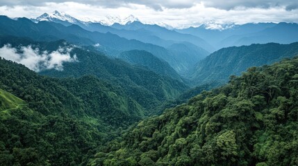 Obraz premium Breathtaking Aerial View of Lush Green Mountainous Landscape with Cloud Cover and Snow-Capped Peaks in the Distance Under a Dramatic Sky