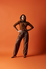 A young woman with braids stands confidently in a studio, showcasing her fashionable outfit against a warm backdrop.