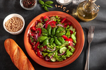 Fresh salad with tomatoes, cucumbers, onions, basil and pine nuts. A plate of salad on a dark...
